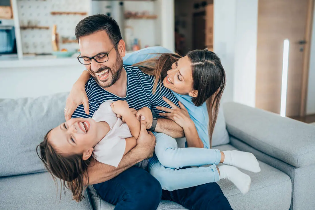 Family laughing together on the couch — family wellbeing and child therapy supports